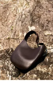 Macro detail of dark brown pebble leather texture on a minimalist hobo crescent bag
