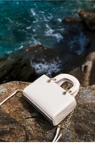 Détail du sac à main en cuir blanc à texture crocodile avec anneaux et chaîne dorés