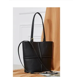 Detail of black pebbled leather tote bag featuring cross-stitched design and golden hardware