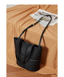Detail of black pebbled leather tote bag with gold hardware on warm fabric background