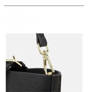 Detailed close-up of golden metal hooks and lychee grain leather on a black tote bag