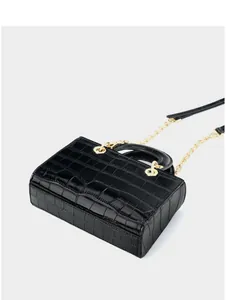 Détail du sac à main en cuir noir brillant effet crocodile avec boucles dorées