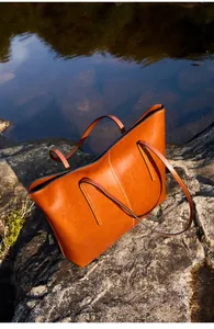 Close-up of a brown leather tote bag with lychee texture on a scenic water rock