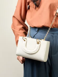 Sac à main blanc cassé avec texture crocodile et chaîne dorée porté sur un modèle
