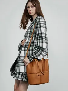 Brown leather tote bag with cross-stitch design and adjustable shoulder strap worn by model