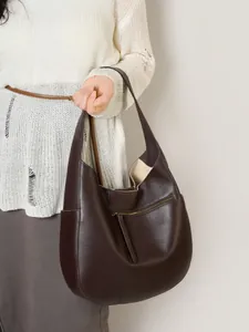 Large dark brown leather crescent hobo tote bag shown held by a model in a white sweater
