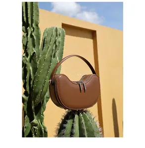 Detailed view of a brown leather crescent handbag placed on a cactus under blue sky
