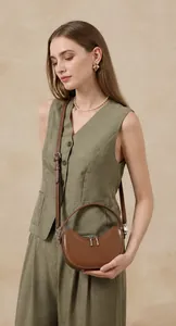 Detail of a brown leather crescent shoulder bag styled with a green sleeveless blazer