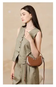 Detail of brown leather crescent bag featuring dual zippers and detachable shoulder strap