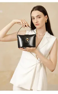 Model holding a structured black leather handbag with a signature golden capsule lock