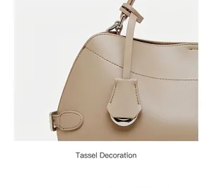 Détail du côté d'un sac en cuir beige avec coutures, boucle en métal et pendentif déco
