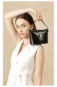 Detail of a black leather handbag featuring a golden capsule lock and sturdy top handle