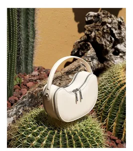 Detail of cream leather dumpling bag with silver zippers placed on a cactus plant