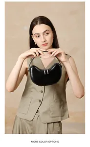 Detail of a minimalist black crescent handbag shown by a model wearing a green vest