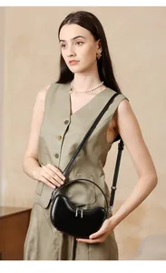 Detail of a minimalist black leather half-moon handbag worn by model in a soft studio setting