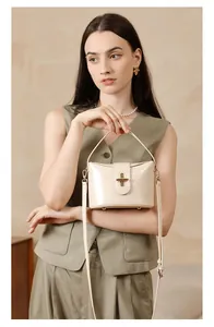Detail of cream leather handbag featuring gold capsule lock and top handle on model
