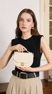Chic beige leather crescent handbag with gold metal clasp held by model in natural light
