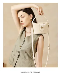 Detail of a cream leather crossbody bag with a distinctive golden arch-shaped metal lock