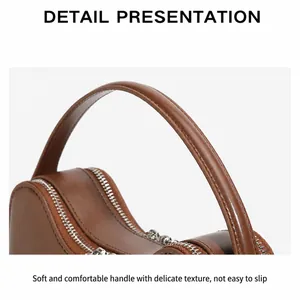 Detailed close-up of brown leather bag showing silver metal zippers and premium stitching