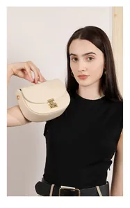 Close-up of cream leather saddle bag with gold metal clasp and top handle on a model