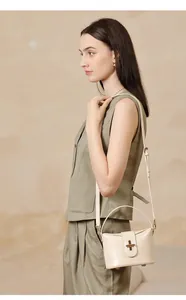 Detail of a beige leather handbag featuring a golden capsule lock and adjustable strap