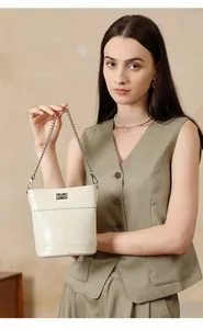Détail d'un sac seau en cuir crème avec chaîne en métal argenté et fermoir pivotant
