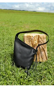 Dettaglio borsa a gnocco in pelle nera con trama litchi e coulisse su erba naturale