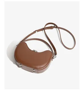 Detail of caramel leather crescent bag featuring silver bottom studs and adjustable strap