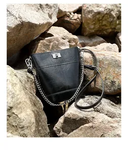 Détail d'un sac seau vintage en cuir noir avec fermoir argenté sur fond de pierre