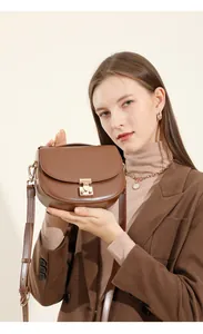 Close-up of brown leather saddle bag with gold metal clasp and adjustable strap