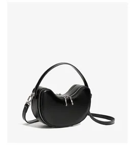Detailed close-up of a minimalist black leather dumpling bag with silver zippers and strap
