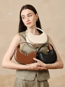 Three premium leather crescent bags in white, brown, and black colors held by a model