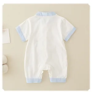 Back view of a white cotton newborn baby romper with blue trim on a beige fabric