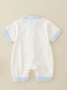 Short sleeve newborn cotton romper in white and blue trim, flat lay on warm beige surface