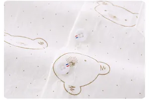 Detail of baby shirt with cartoon bear print and striped edge buttons on white fabric