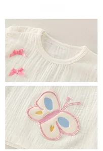 Détail d'un haut bébé en coton avec nœuds en soie rose et broderie papillon multicolore
