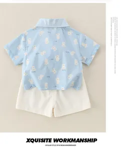 Flat lay of cotton baby boy summer set with light blue bear print shirt and white shorts