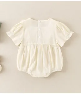 Close-up of cream baby romper with puff sleeves and wood ear trim on cotton fabric