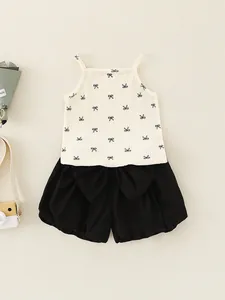 Zomershirt voor baby meisjes met strikjes en zwarte pofbroek op een beige ondergrond