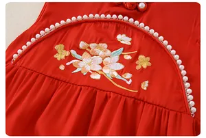Detail of red baby romper with floral embroidery, white pearls, and pleated fabric