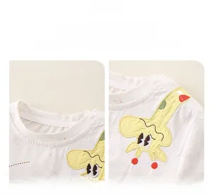 Detail of white cotton baby top featuring yellow giraffe embroidery and shoulder buttons