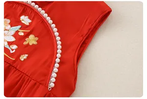 Detailed macro shot of red silk baby romper with floral embroidery and pearl trim accents