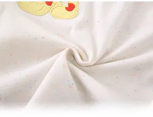 Close-up of soft white cotton fabric with colorful specks and yellow polka dot patch