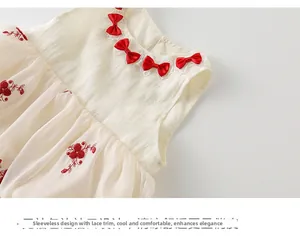 Détail de robe bébé en coton sans manches avec nœuds rouges et broderies florales