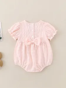 Pagliaccetto rosa per neonata con maniche a sbuffo e fiocco sul retro su sfondo beige