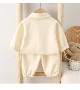 Detailed view of cream-colored baby fleece tracksuit set on a rustic wooden hanger