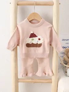 Rosa gestricktes Baby-Set mit Tortenstickerei und Schlaghose an einer Holzleiter präsentiert