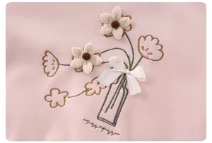 Detail of pink cotton baby top featuring 3D plush flowers and floral embroidery