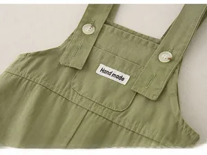 Detail of green cotton overalls featuring a textured chest pocket and vintage white buttons