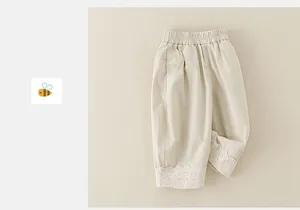 Detailed view of elastic waistband and delicate white lace embroidery on beige toddler pants